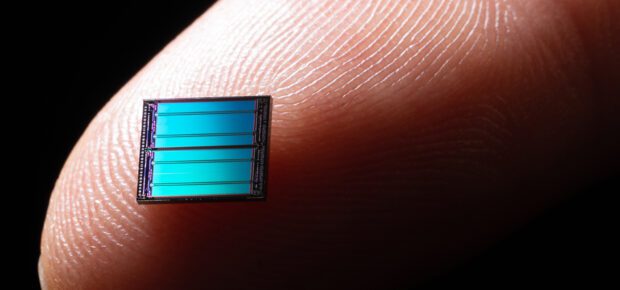 Blue Colored Computer Chip on Tip of Index Finger Against Dark Black Background Extreme Close-up View, Macro Photo.