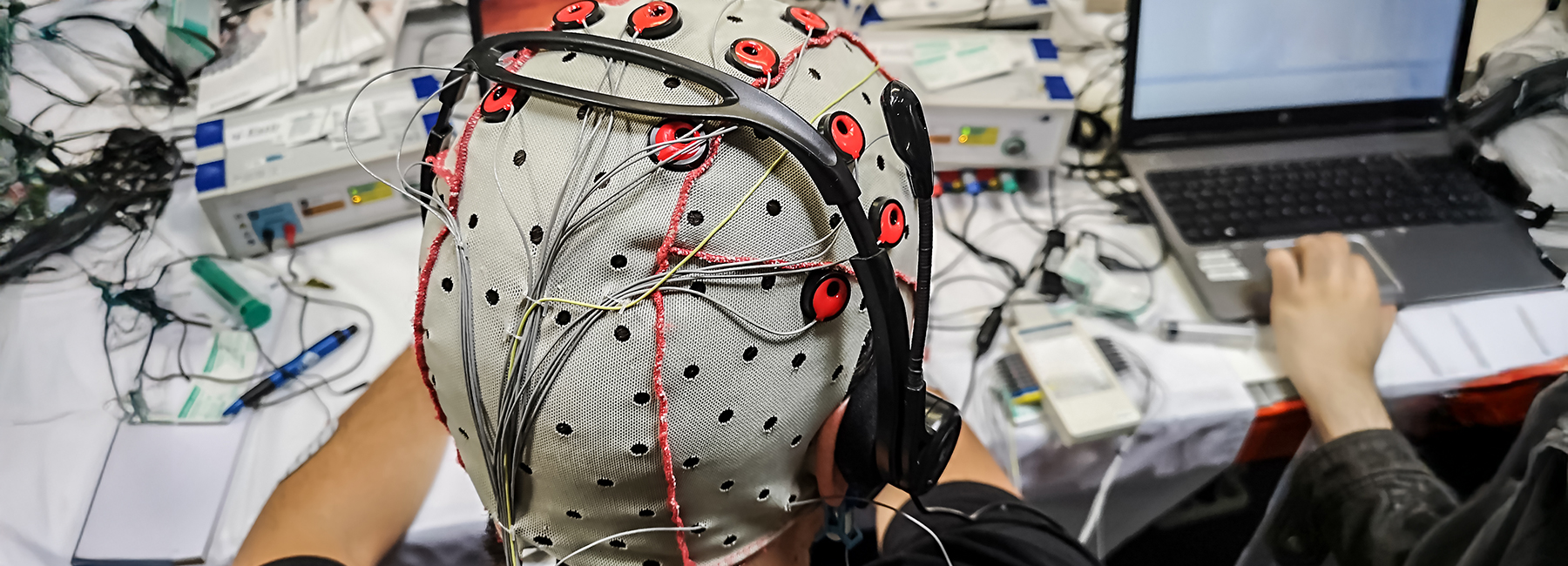 The electroencephalogram (EEG) head cap with flat metal discs (electrodes) in a science lab with laptops blurred at the background