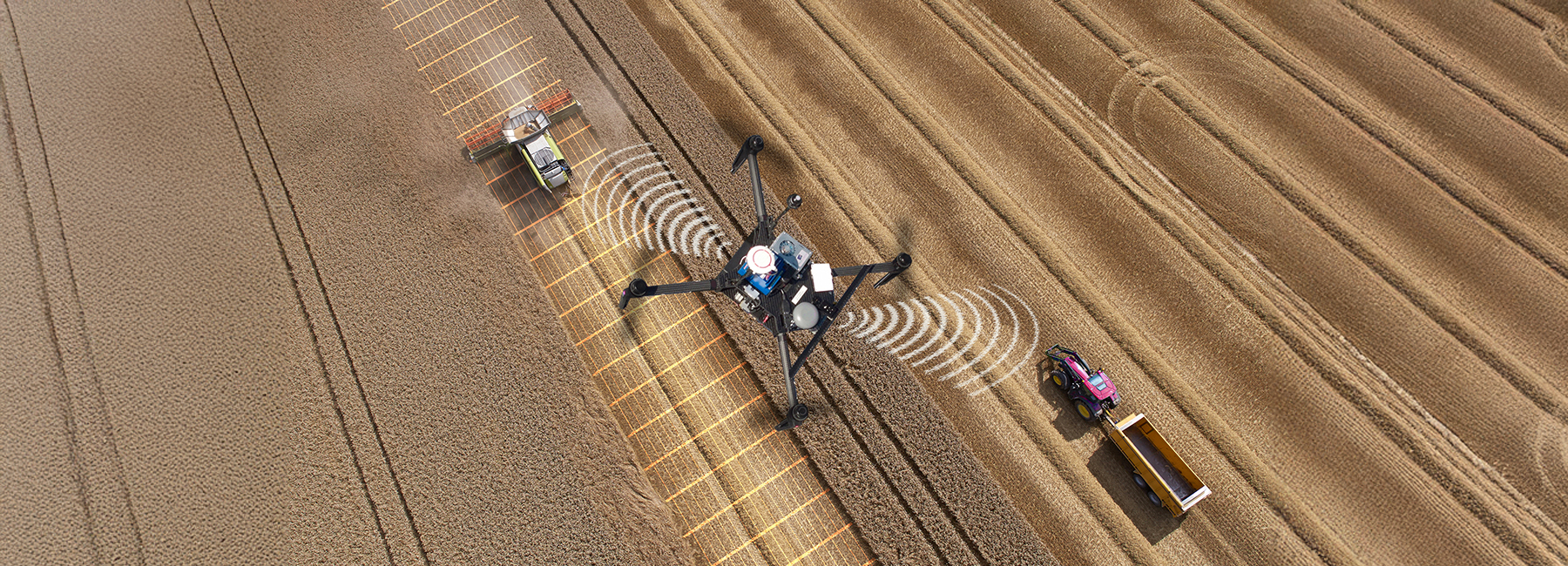 Overhead aerial view of a drone communicating with a combine harvester and tractor while harvesting a crop